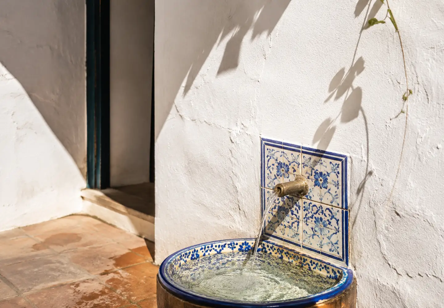 Fuente de azulejos azules y latón en un patio blanco iluminado por el sol de Cádiz
